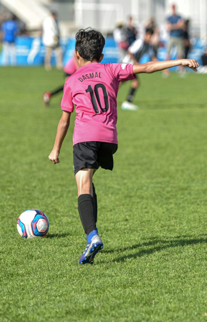 Smartly kitted young boy sets up to kick a soccer ball down a green field.
